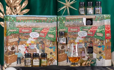 "Cartoon-style whisky advent calendar with festive market scenes and small whisky bottles displayed in front."