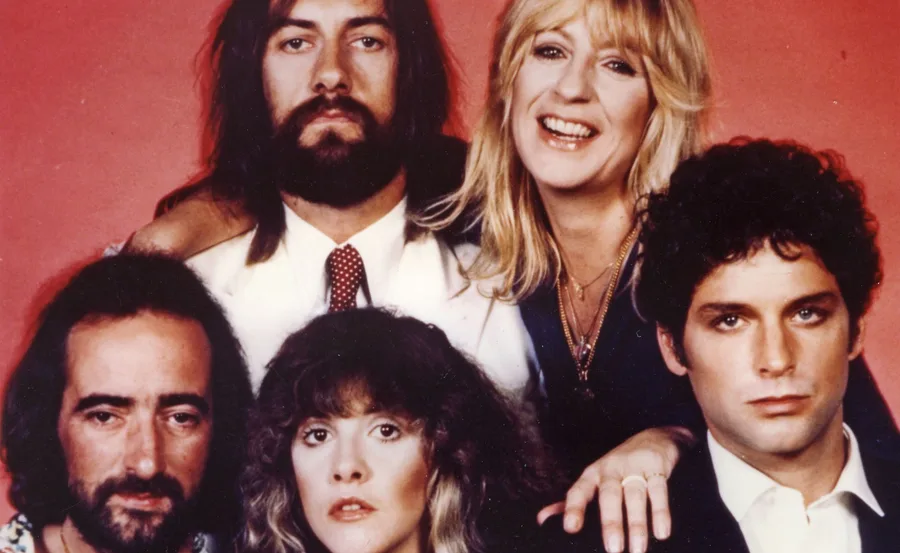 Five members of Fleetwood Mac posing together against a red background.