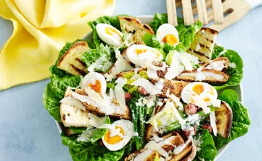 Chicken and cos Caesar salad with boiled eggs, croutons, Parmesan, and creamy dressing on a plate with a yellow napkin.