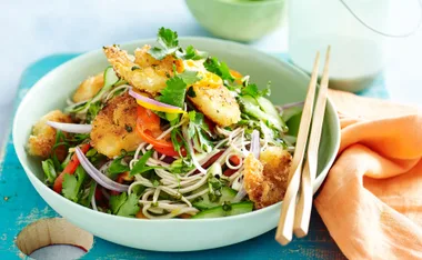 Crispy prawn and cucumber salad with noodles, herbs, and vibrant vegetables in a green bowl, garnished with cilantro.