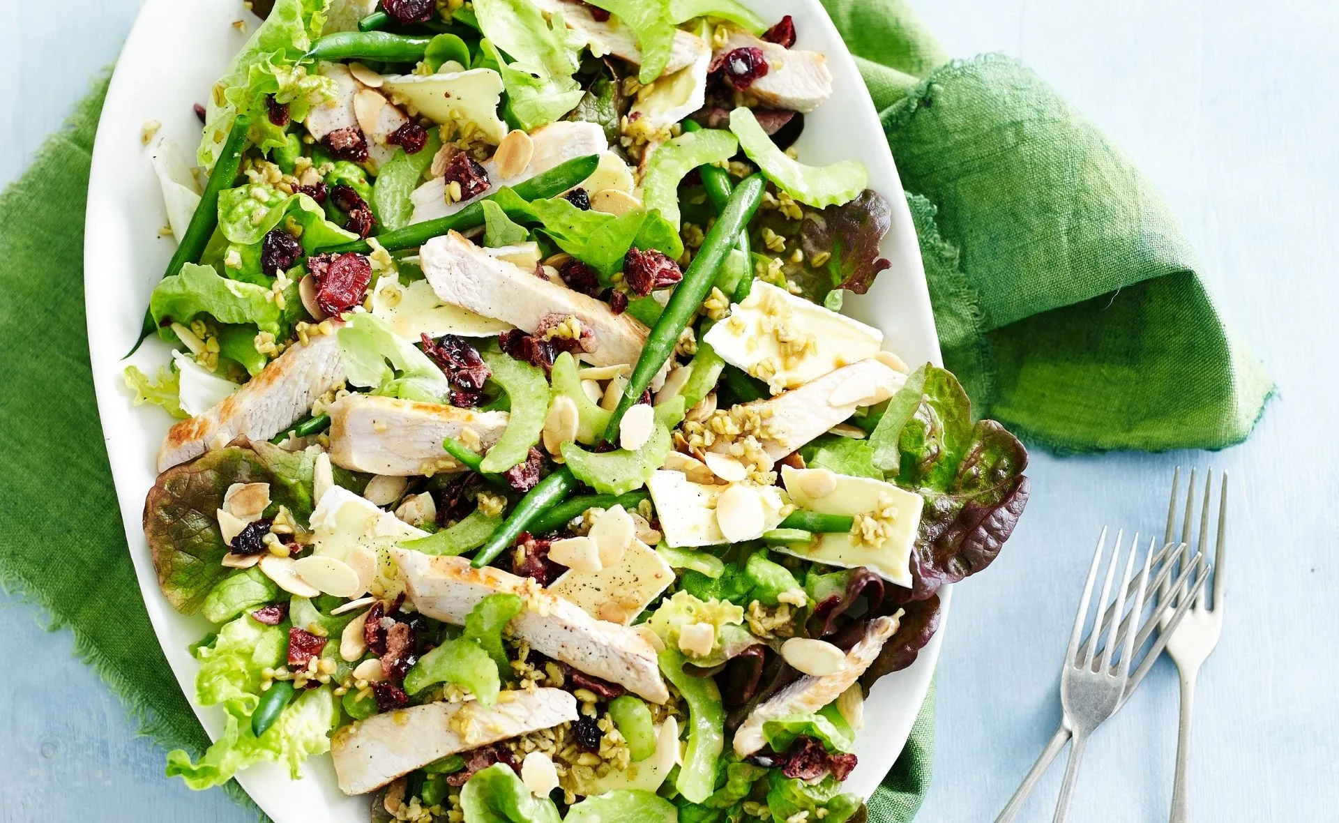 Turkey, cherry, and almond salad with mixed greens on a white plate, placed on a green napkin.