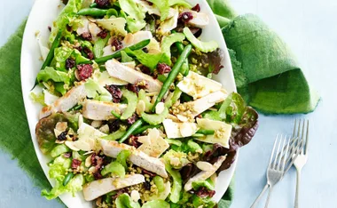 Turkey, cherry, and almond salad with mixed greens on a white plate, placed on a green napkin.