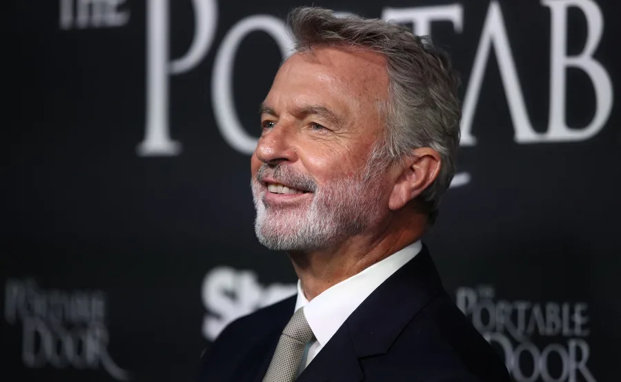 A smiling man with gray hair and beard in a suit at "The Portable Door" event.