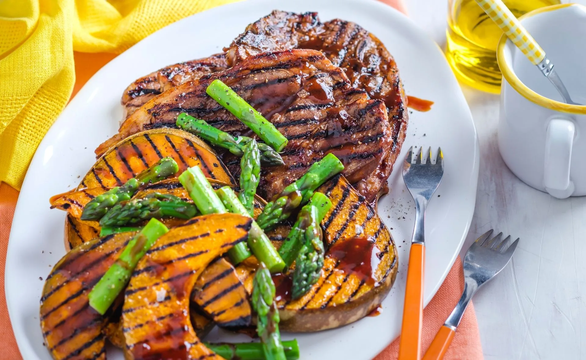 Grilled hoisin lamb chops with sesame pumpkin slices and fresh asparagus on a white plate.