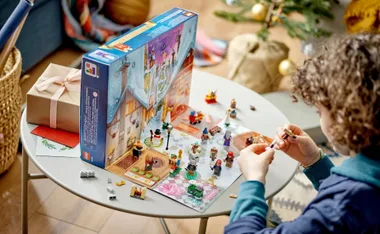 Child assembling LEGO Harry Potter advent calendar on table, with figures and gift box nearby.