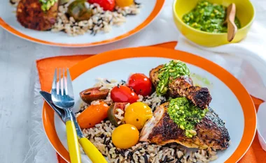 Plate of chicken with pesto, colorful cherry tomatoes, and wild rice on an orange-trimmed dish.