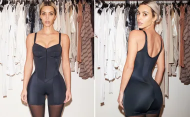Woman wearing black shapewear in front of a closet with various clothes hanging.