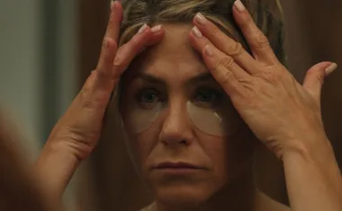 Woman wearing under-eye patches, pressing palms to forehead, looking in mirror.