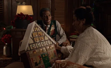 Two people examining a large, house-shaped advent calendar in a cozy, festive room adorned with Christmas decorations.