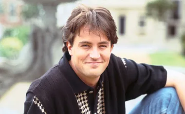 A person wearing a black and white patterned shirt, smiling outdoors.