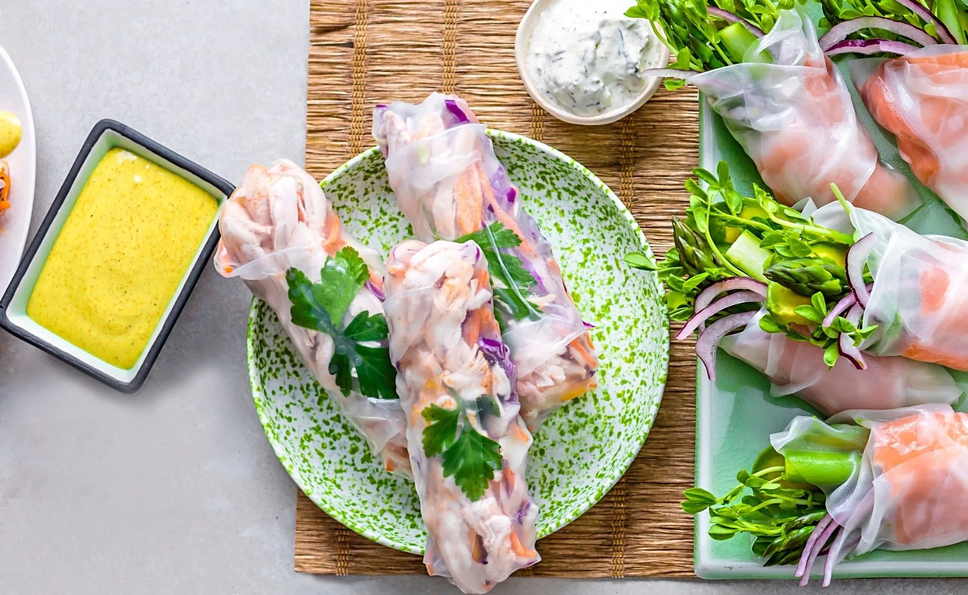 Fresh rice paper rolls with chicken, mango, and herbs on a plate, served with dipping sauces.