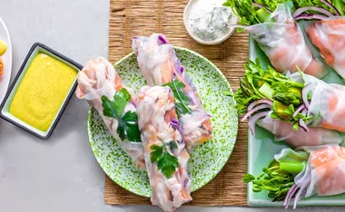 Fresh rice paper rolls with chicken, mango, and herbs on a plate, served with dipping sauces.