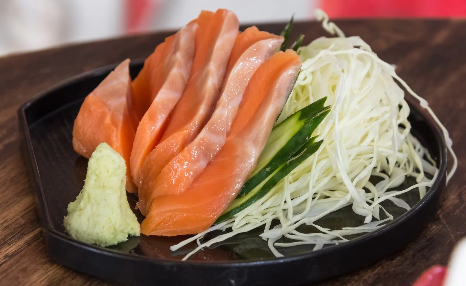 Fresh salmon slices on a plate with shredded cabbage, cucumber, and a dollop of wasabi for garnish.