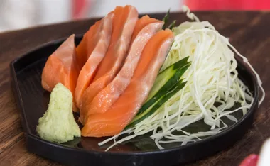 Fresh salmon slices on a plate with shredded cabbage, cucumber, and a dollop of wasabi for garnish.