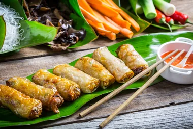 Fresh Vietnamese spring rolls with rice paper, served with dipping sauce, on a banana leaf with chopsticks.