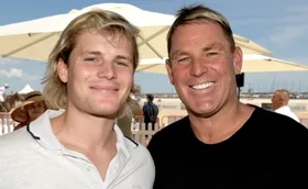 Two smiling people posing together outdoors under a sun umbrella.