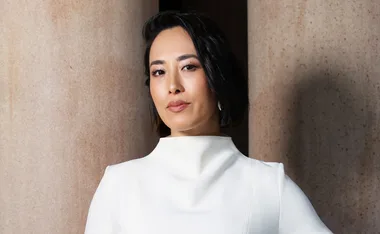 A person with short black hair wearing a white outfit, standing in front of large columns.