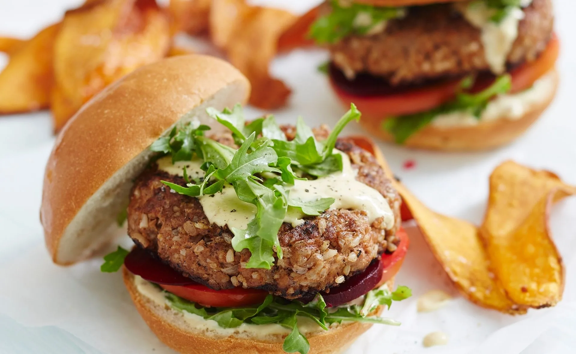 Beef and brown rice burger garnished with arugula and cream sauce, served with vegetable chips.
