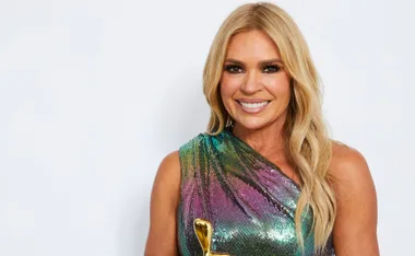 Person smiling, wearing a colorful sequin dress, holding a gold award.