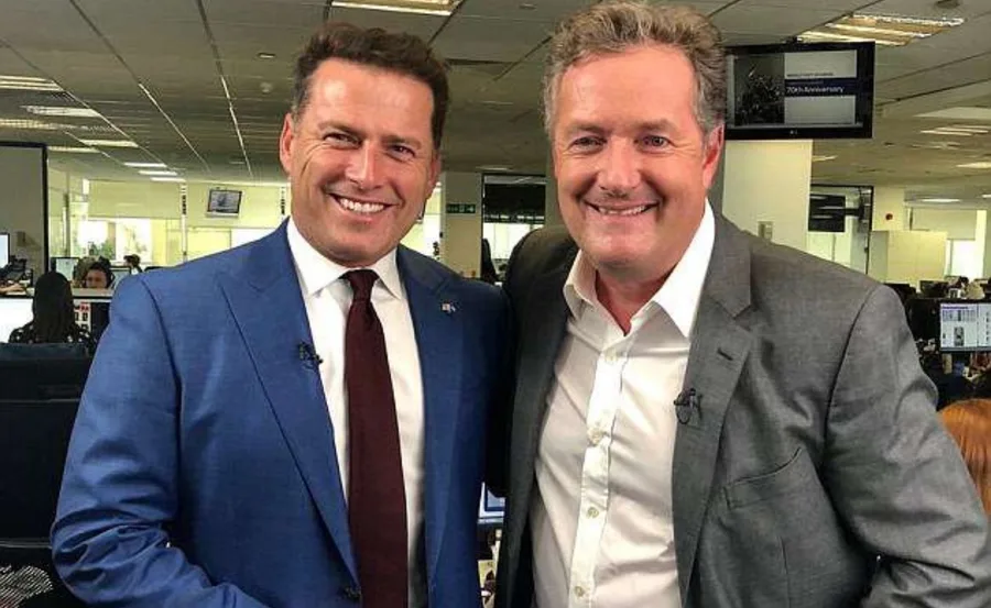 Two men smiling and posing in an office setting, both wearing suits.