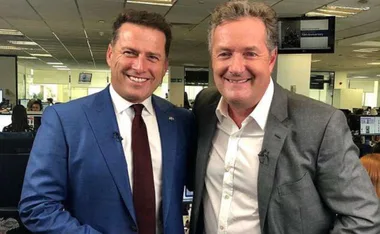 Two men smiling and posing in an office setting, both wearing suits.