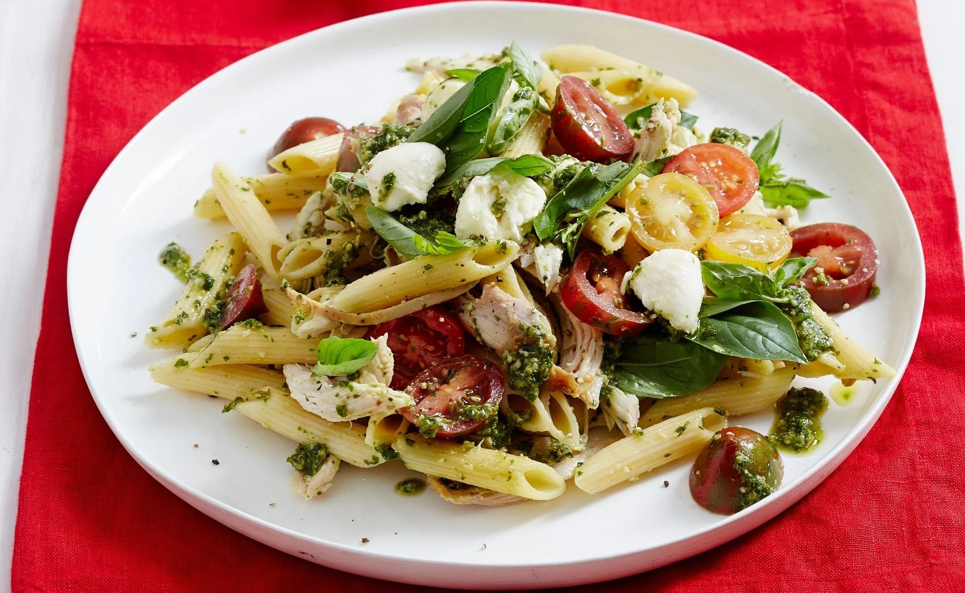 Caprese chicken pasta salad with penne, cherry tomatoes, basil, mozzarella, and pesto on a white plate.