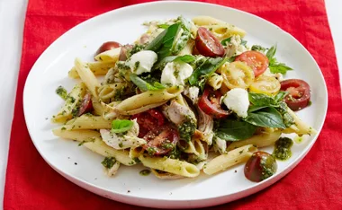 Caprese chicken pasta salad with penne, cherry tomatoes, basil, mozzarella, and pesto on a white plate.