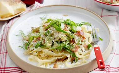 Plate of fettuccine with sliced asparagus, broad beans, and fennel, garnished with grated cheese and a red-handled fork.