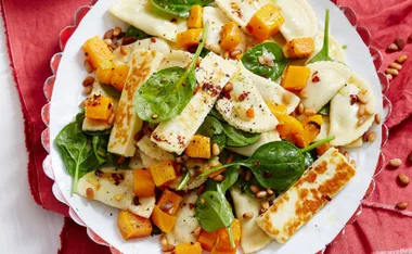 Pumpkin, halloumi, and pine nut pasta salad with spinach on a white plate.