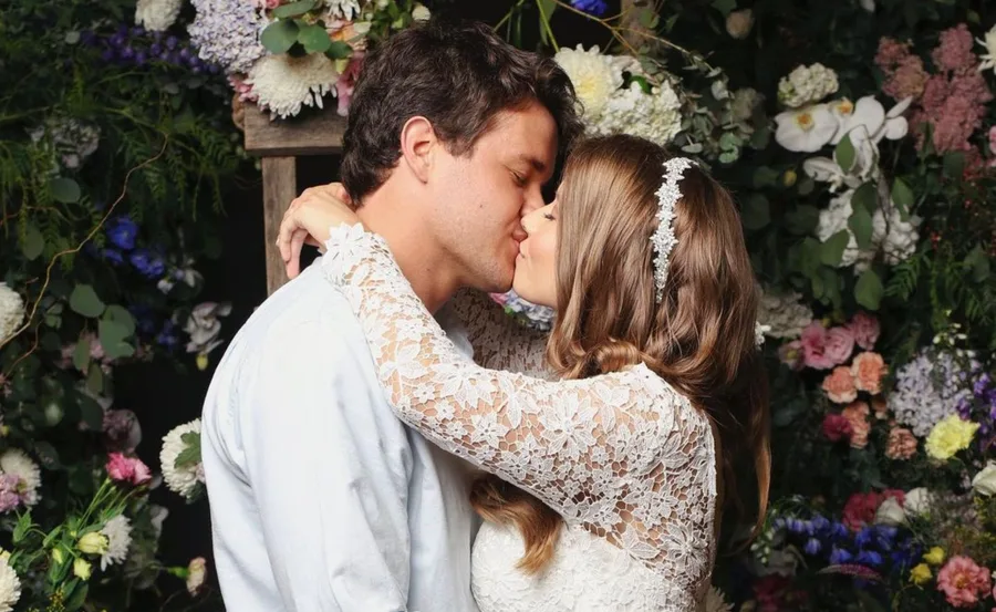 Couple kissing at their wedding surrounded by colorful flowers, bride in lace dress with floral headband.