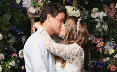 Couple kissing at their wedding surrounded by colorful flowers, bride in lace dress with floral headband.