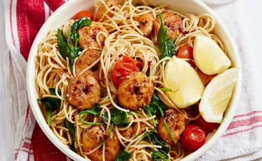 Spaghettini with garlic, chilli prawns, spinach, cherry tomatoes, and lemon wedges in a bowl.
