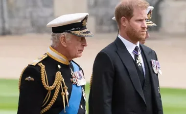 King Charles in uniform and Prince Harry in a suit, both wearing medals, walking side by side.