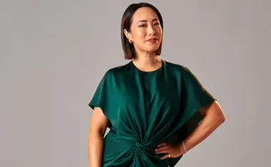 A woman in a green, knotted dress poses confidently against a gray background.