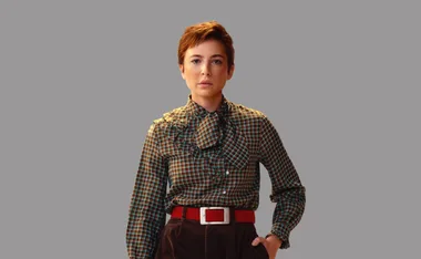 A person wearing a plaid shirt with puff sleeves and a red belt, standing against a gray background.