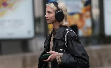 Young woman wearing black over-ear headphones and holding a smartphone, walking outdoors.