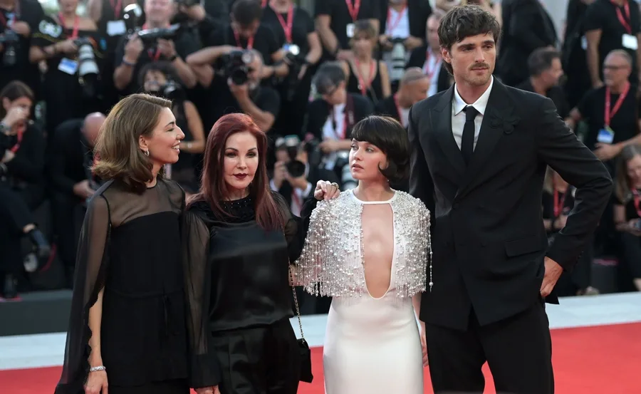 Four people pose on the red carpet at the premiere of the movie "Priscilla" with photographers in the background.