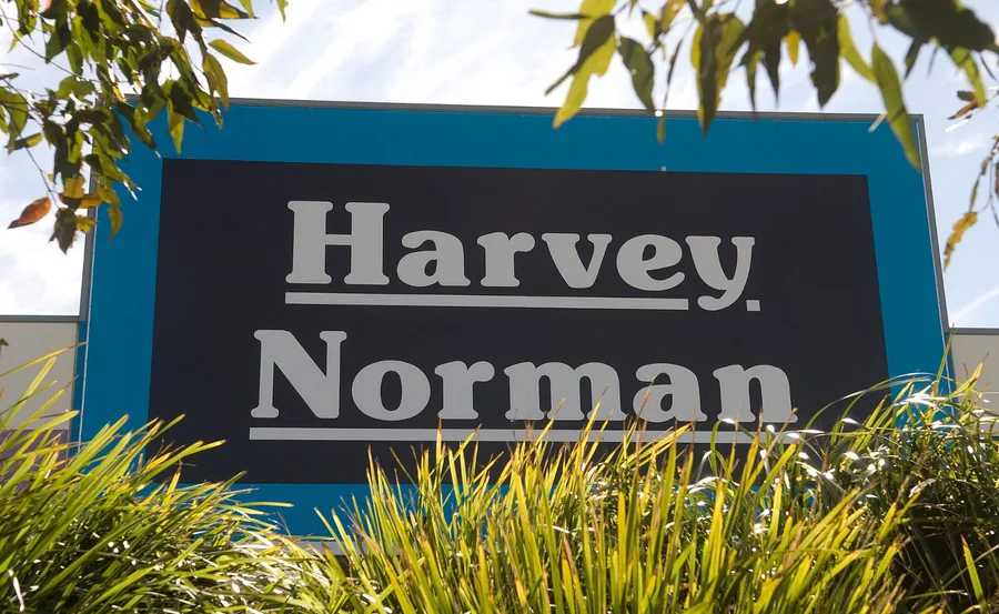 "Harvey Norman store sign with surrounding foliage under a clear sky."