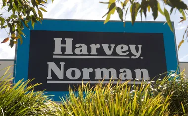 "Harvey Norman store sign with surrounding foliage under a clear sky."