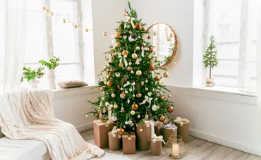 Christmas tree with gold and white ornaments, surrounded by wrapped gifts, in a bright room with festive decor.