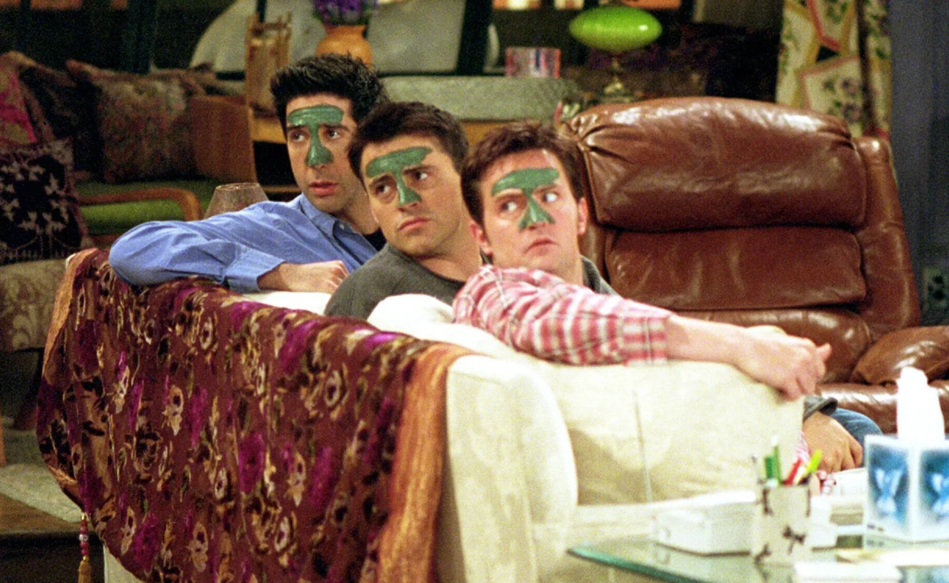 Three people on a couch with green face masks on their noses in a living room setting.
