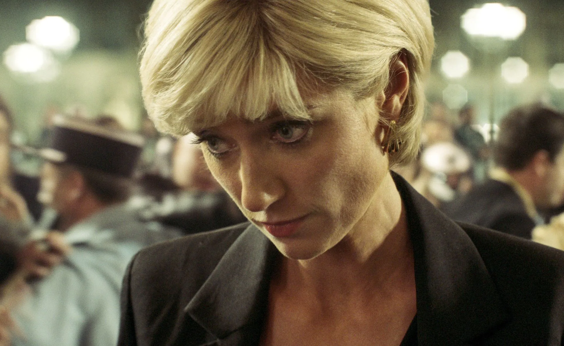 A woman with short blonde hair and focused expression in a crowded setting.
