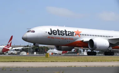 Jetstar airplane landing on runway with another airplane in the background.