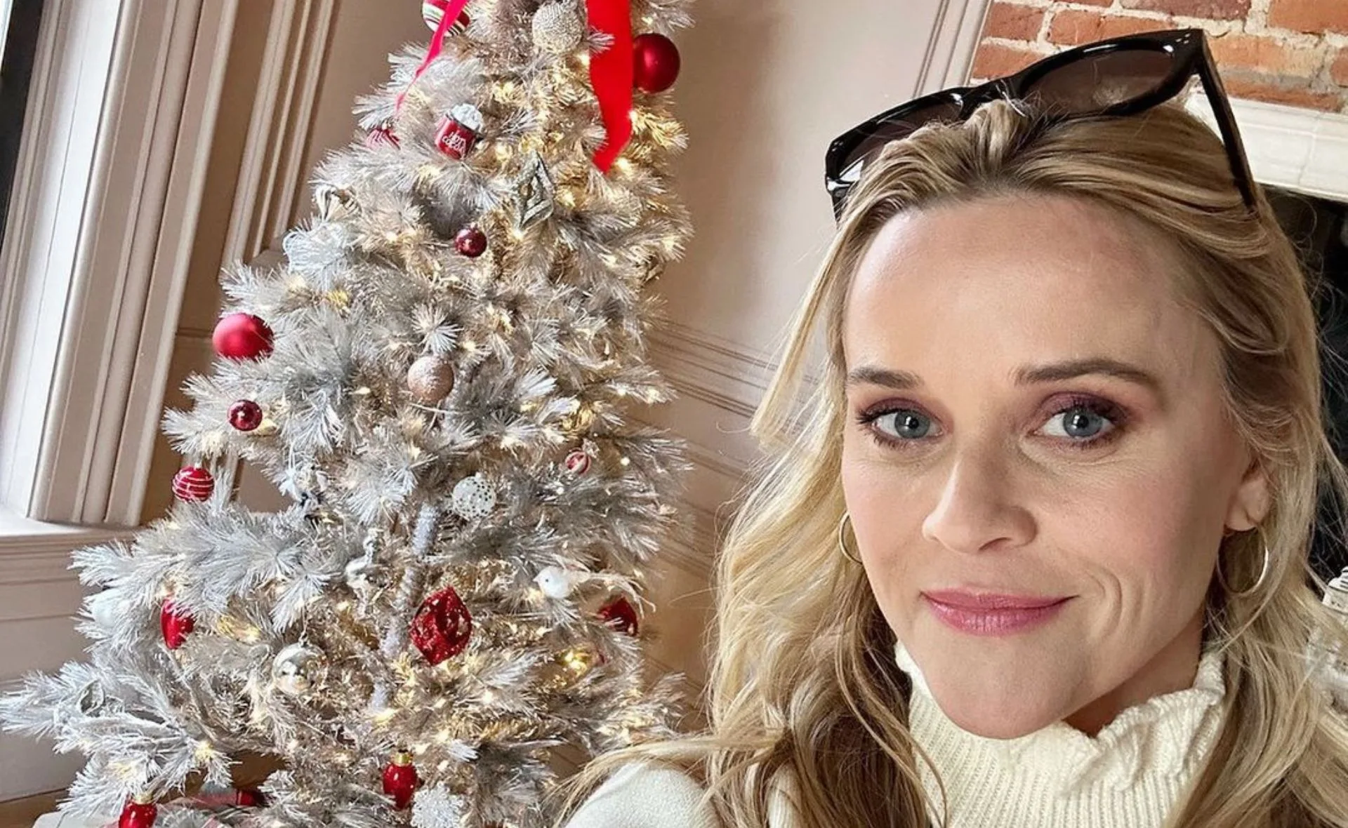 Person taking a selfie next to a decorated Christmas tree with lights and ornaments.