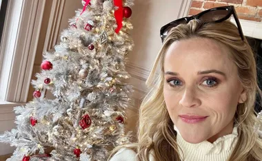 Person taking a selfie next to a decorated Christmas tree with lights and ornaments.
