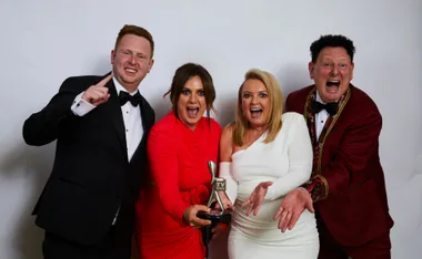 Four people in formal attire excitedly holding a TV Week award, smiling at the camera.