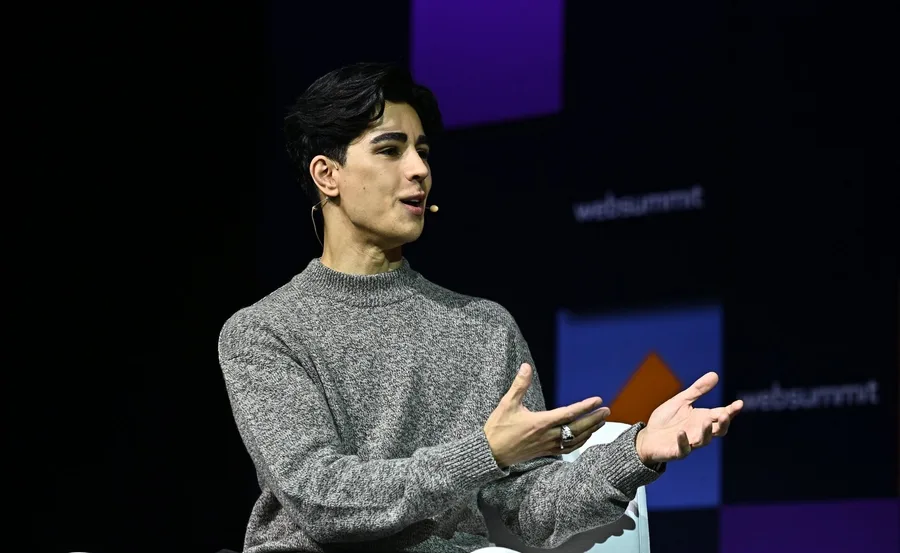 A person speaking on stage with a headset mic, wearing a gray sweater, at a conference event with 'websummit' logo.