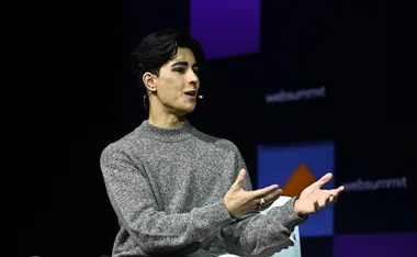 A person speaking on stage with a headset mic, wearing a gray sweater, at a conference event with 'websummit' logo.
