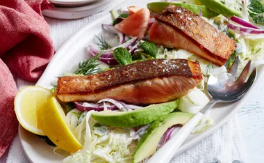 Crispy salmon fillets on creamy cabbage with avocado and lemon wedges, served on a white plate.