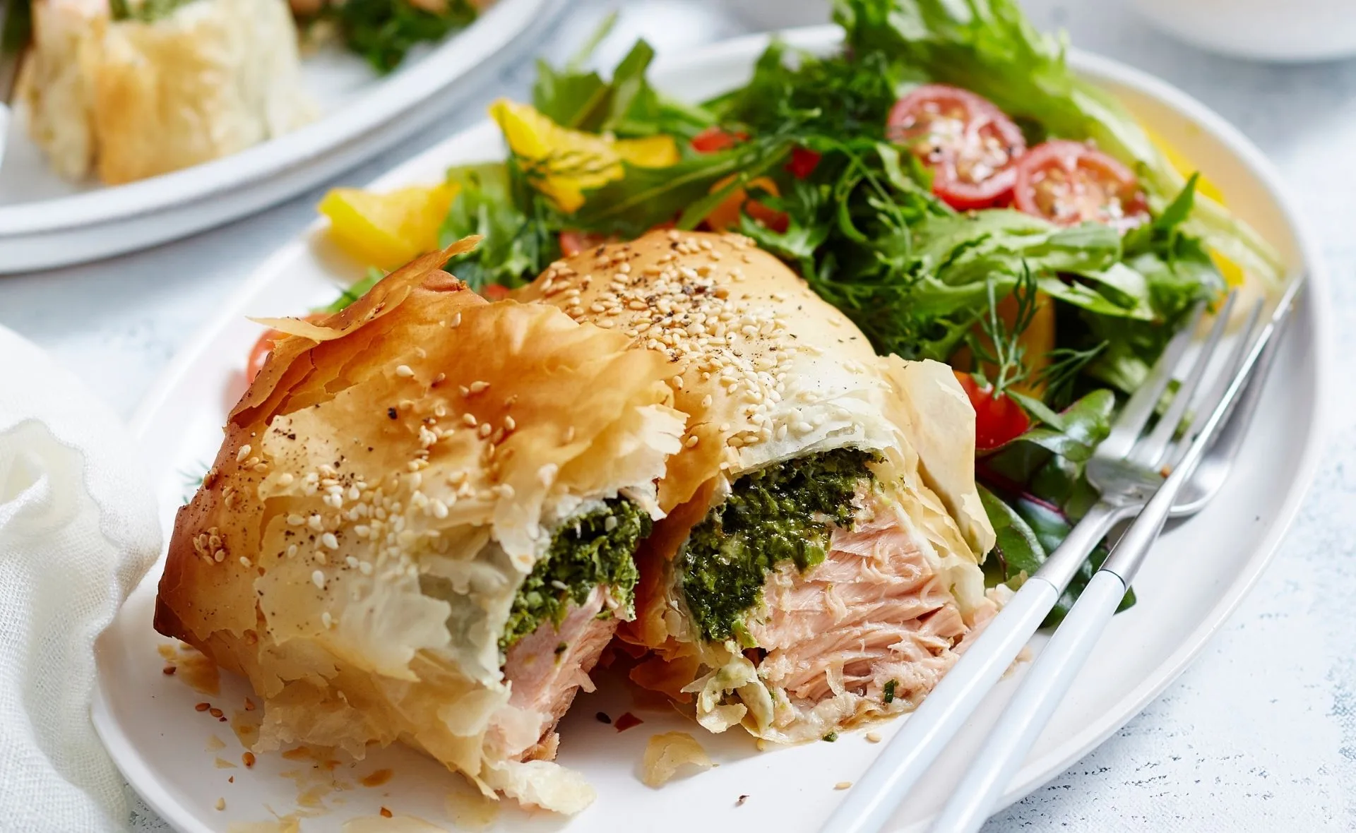 Baked salmon and spinach feta parcel with mixed greens on a white plate.